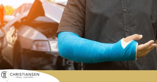 man with a broken arm in front of a crashed car